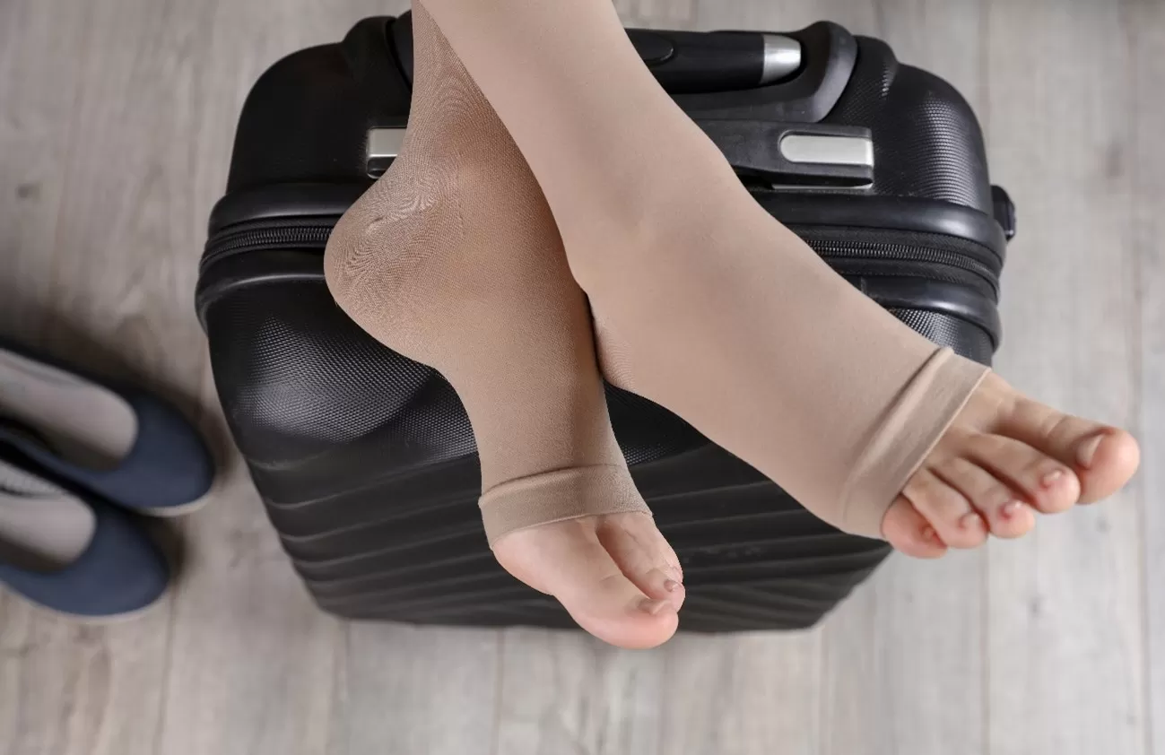 Pés vestindo meias de compressão descansando em cima de uma mala de viagem